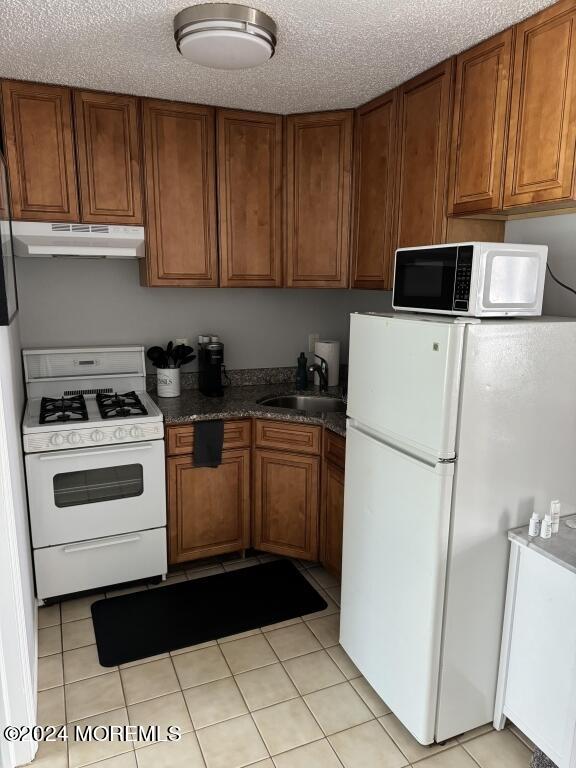 kitchen with a textured ceiling, sink, white appliances, and light tile patterned flooring