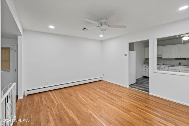 unfurnished room featuring light hardwood / wood-style flooring, a baseboard heating unit, ceiling fan, and sink