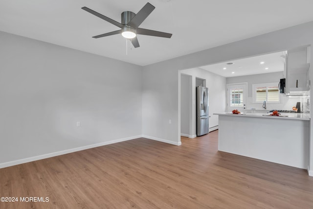 kitchen featuring light wood-type flooring, ceiling fan, white cabinets, stainless steel fridge, and kitchen peninsula