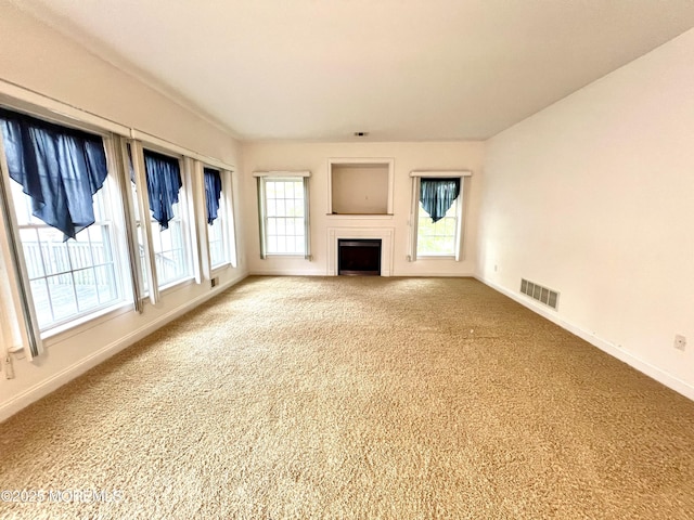 unfurnished living room featuring carpet flooring, baseboards, visible vents, and a wealth of natural light