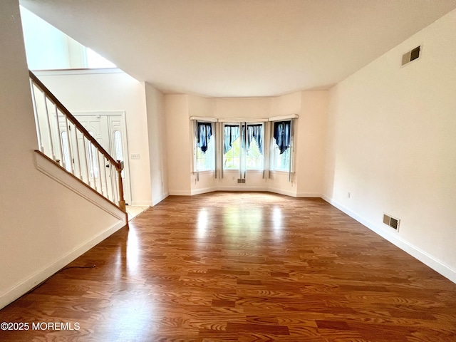 unfurnished living room with stairway, baseboards, wood finished floors, and visible vents