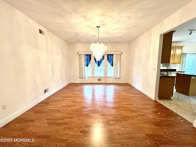 unfurnished dining area with visible vents, baseboards, wood finished floors, and a notable chandelier