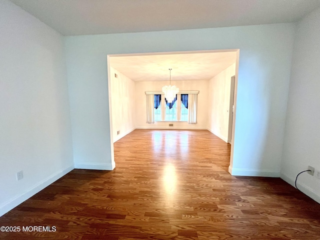 unfurnished dining area featuring baseboards, wood finished floors, and a notable chandelier