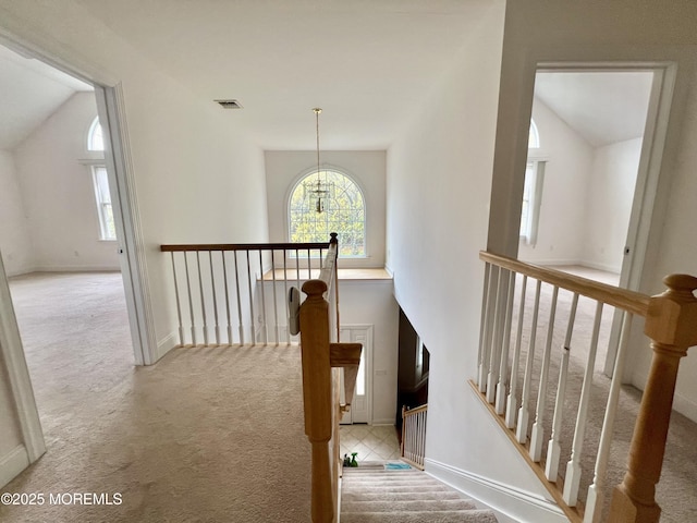 corridor with visible vents, vaulted ceiling, an upstairs landing, a chandelier, and carpet flooring
