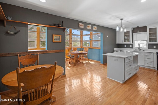 kitchen with light wood-type flooring, hanging light fixtures, a kitchen island, and white cabinets