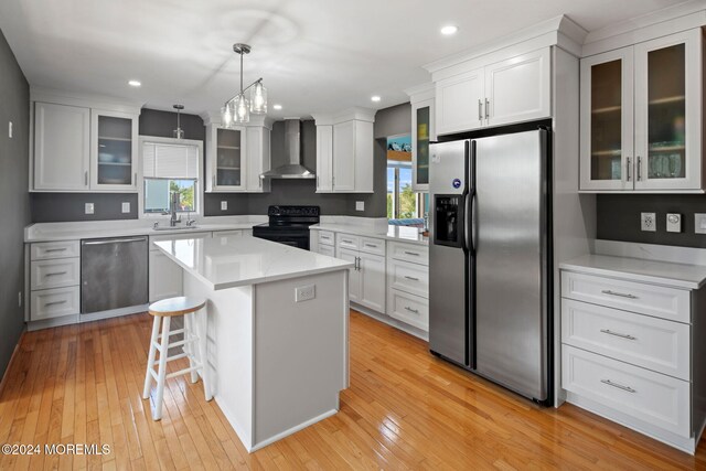 kitchen with appliances with stainless steel finishes, light hardwood / wood-style floors, wall chimney exhaust hood, a kitchen island, and pendant lighting