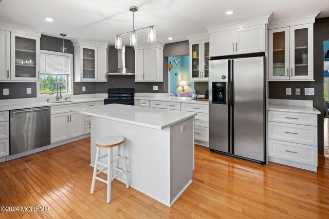 kitchen featuring hanging light fixtures, a kitchen island, wall chimney exhaust hood, light hardwood / wood-style flooring, and appliances with stainless steel finishes