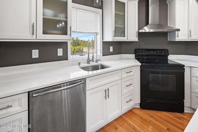 kitchen featuring black range with electric stovetop, wall chimney exhaust hood, white cabinetry, dishwasher, and light wood-type flooring