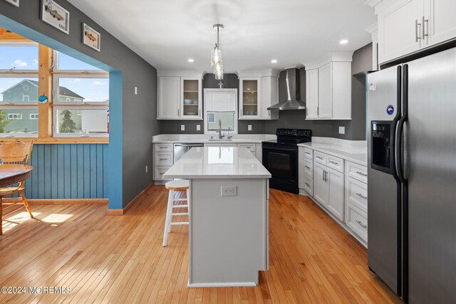 kitchen with a center island, sink, wall chimney range hood, appliances with stainless steel finishes, and decorative light fixtures