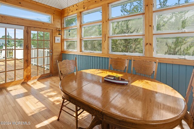 dining area featuring light wood-type flooring, wooden walls, and a wealth of natural light