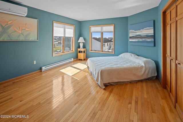 bedroom with a baseboard heating unit, a closet, light wood-type flooring, and a wall mounted AC