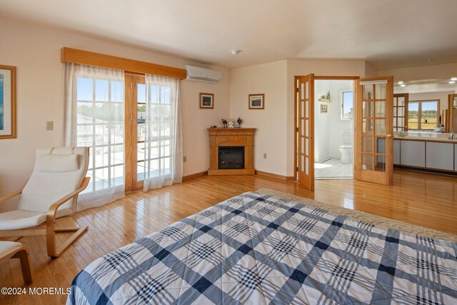 bedroom featuring light hardwood / wood-style flooring, ensuite bath, french doors, and a wall mounted AC