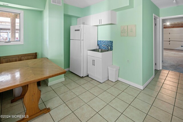 kitchen featuring white cabinets, backsplash, light tile patterned floors, white fridge, and sink