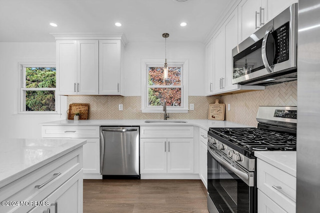 kitchen featuring dark wood-type flooring, white cabinets, hanging light fixtures, sink, and appliances with stainless steel finishes