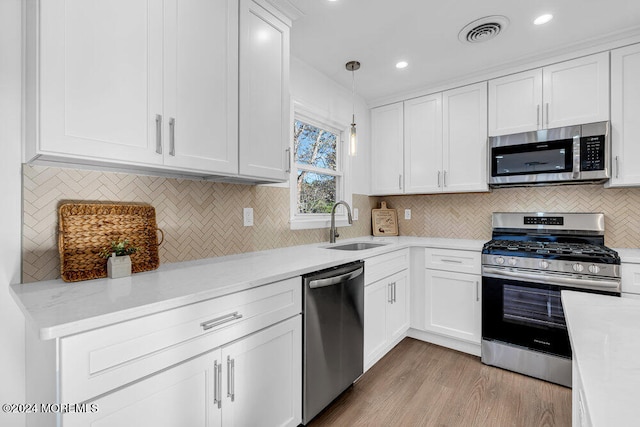 kitchen with stainless steel appliances, sink, decorative light fixtures, white cabinets, and light hardwood / wood-style floors