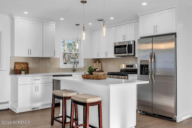 kitchen with hanging light fixtures, stainless steel appliances, a kitchen island, hardwood / wood-style floors, and white cabinets