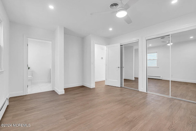 unfurnished bedroom featuring baseboard heating, light hardwood / wood-style flooring, ceiling fan, and multiple closets