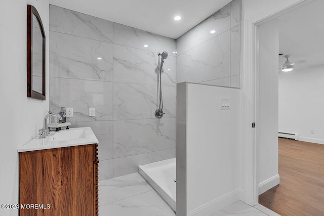 bathroom featuring a tile shower, vanity, ceiling fan, a baseboard heating unit, and hardwood / wood-style flooring