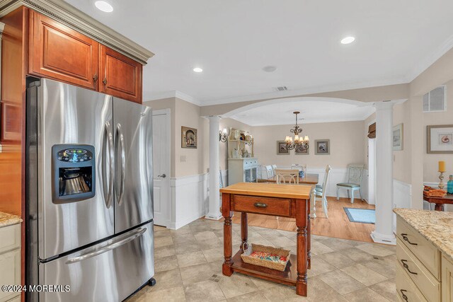 kitchen with ornamental molding, stainless steel refrigerator with ice dispenser, light stone countertops, and decorative columns