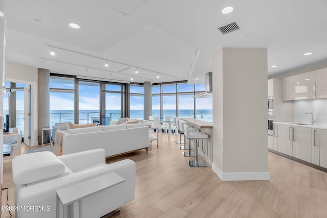 living room featuring floor to ceiling windows, a water view, sink, and light hardwood / wood-style flooring