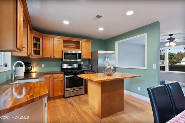 kitchen with a kitchen island, stainless steel appliances, sink, light wood-type flooring, and butcher block countertops