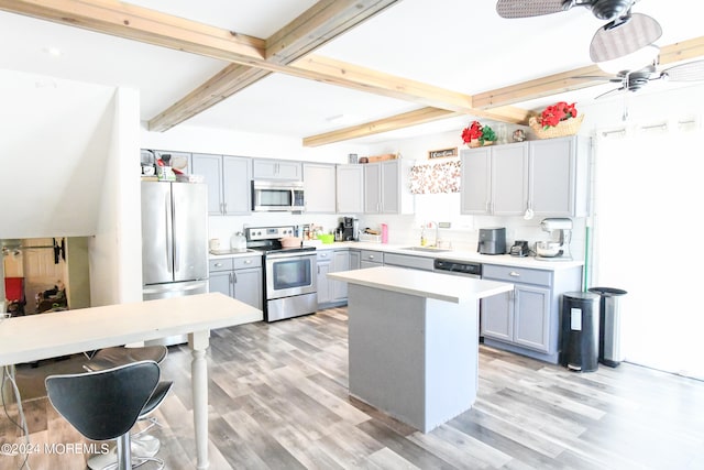 kitchen with appliances with stainless steel finishes, beam ceiling, light hardwood / wood-style floors, and a kitchen island