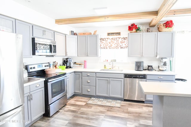 kitchen with light wood-type flooring, beam ceiling, sink, and stainless steel appliances