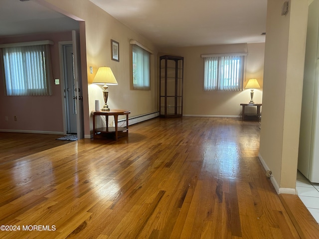 unfurnished living room featuring wood-type flooring and a baseboard heating unit