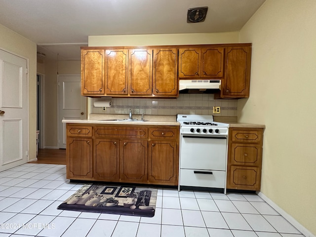 kitchen featuring tasteful backsplash, white gas range, light tile patterned floors, and sink