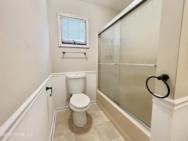 full bathroom with wainscoting, combined bath / shower with glass door, and toilet