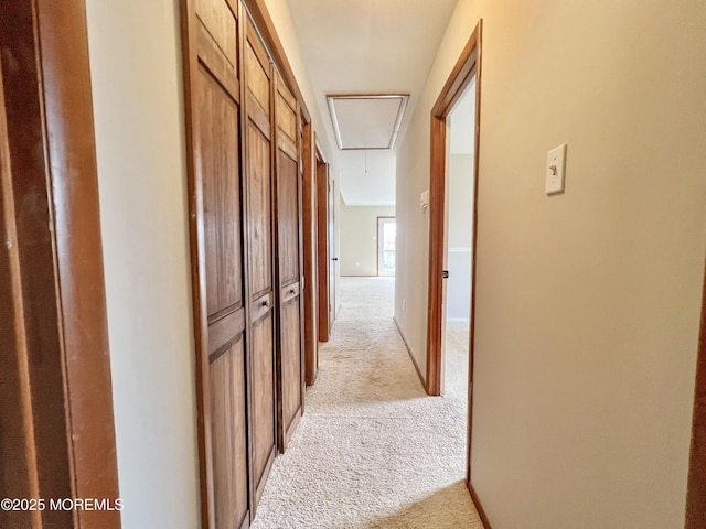 hall featuring attic access, light colored carpet, and baseboards