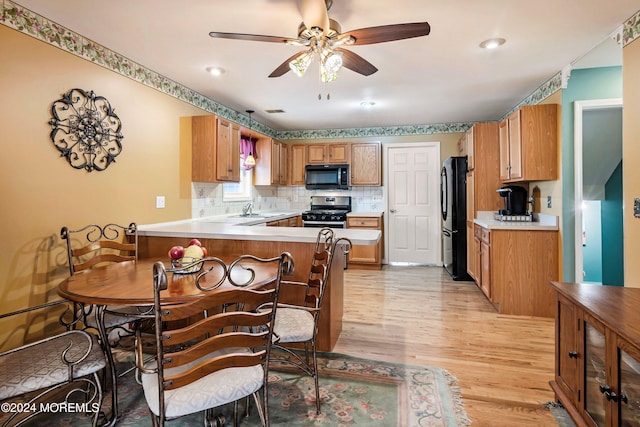 kitchen with light hardwood / wood-style flooring, kitchen peninsula, sink, black appliances, and ceiling fan