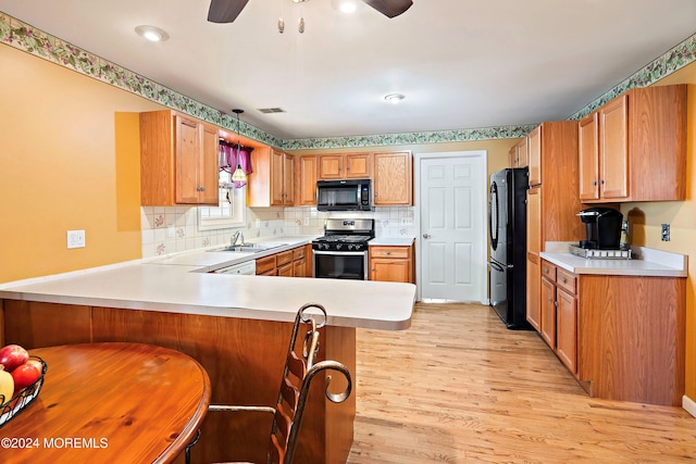 kitchen with kitchen peninsula, sink, black appliances, a kitchen bar, and light hardwood / wood-style floors