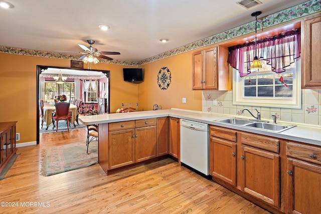 kitchen with sink, dishwasher, kitchen peninsula, pendant lighting, and light hardwood / wood-style flooring