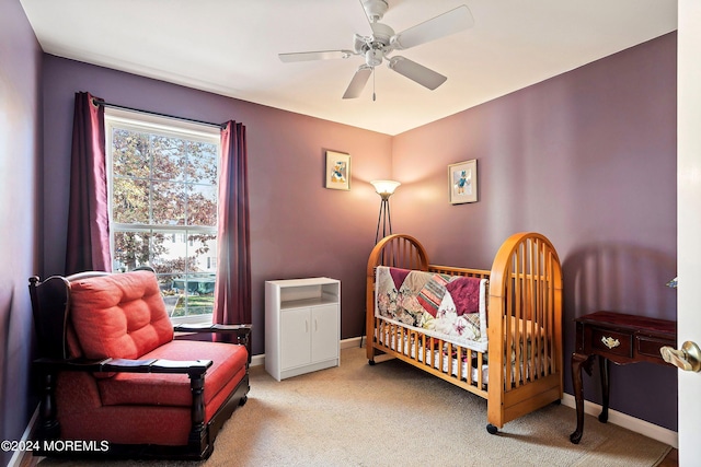 bedroom featuring light carpet, a nursery area, and ceiling fan