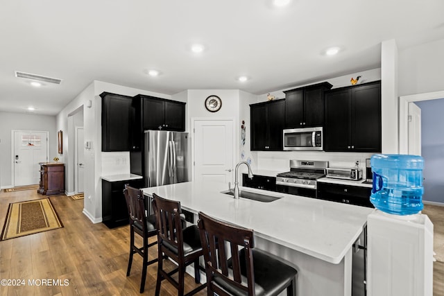 kitchen featuring sink, a breakfast bar area, stainless steel appliances, a center island with sink, and light wood-type flooring