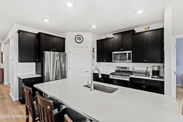 kitchen with a kitchen bar, sink, light hardwood / wood-style flooring, stainless steel appliances, and backsplash