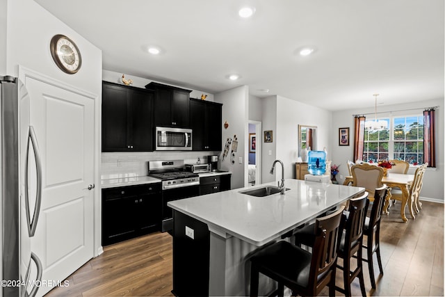 kitchen with sink, hanging light fixtures, a center island with sink, a kitchen breakfast bar, and stainless steel appliances