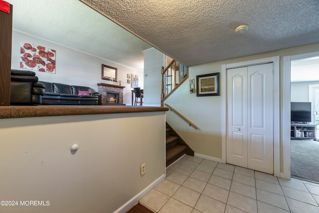 staircase with tile patterned flooring, a textured ceiling, and a stone fireplace