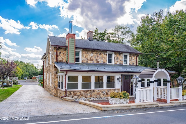 view of front facade featuring stone siding, a chimney, and a high end roof