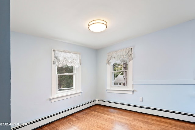 unfurnished room featuring a wealth of natural light, a baseboard radiator, and wood finished floors