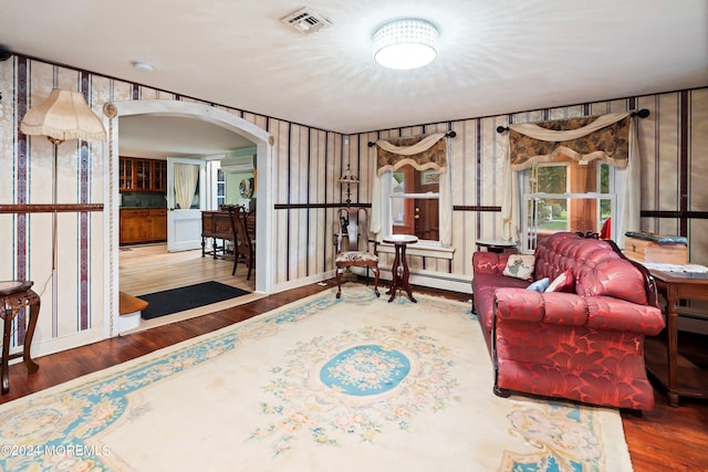 living area featuring arched walkways, a baseboard heating unit, wood finished floors, visible vents, and baseboards