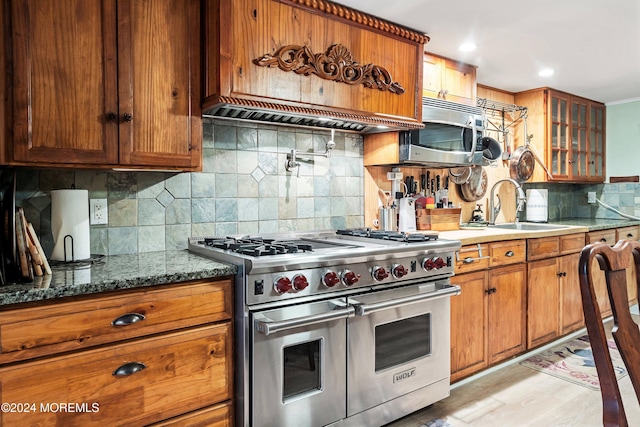 kitchen featuring brown cabinets, stainless steel appliances, tasteful backsplash, glass insert cabinets, and a sink