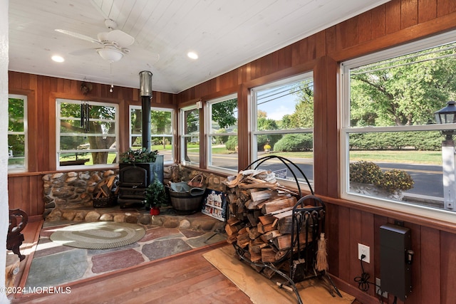 sunroom / solarium featuring a wood stove, wooden ceiling, and ceiling fan