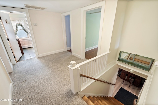 hallway with baseboards, visible vents, an upstairs landing, carpet floors, and a baseboard heating unit