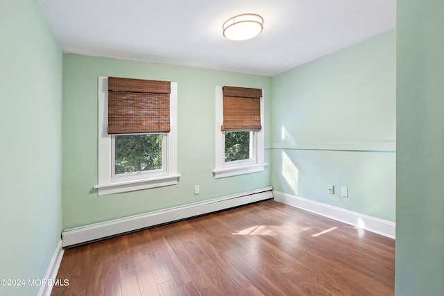 empty room featuring a baseboard radiator, baseboards, and wood finished floors