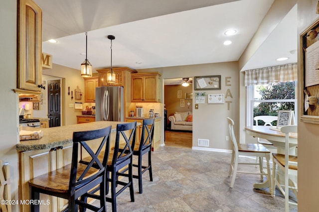 kitchen with stainless steel fridge, ceiling fan, stove, light stone countertops, and decorative light fixtures