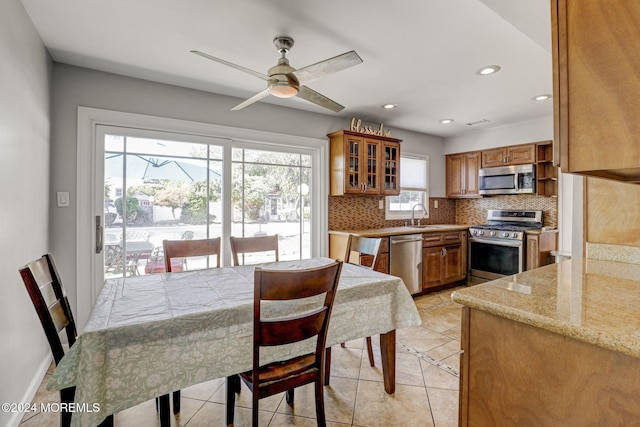 kitchen with light stone counters, ceiling fan, stainless steel appliances, tasteful backsplash, and sink