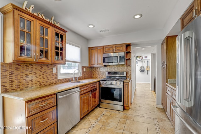 kitchen with light stone countertops, decorative backsplash, sink, light tile patterned flooring, and appliances with stainless steel finishes