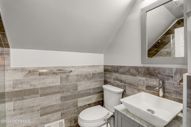 bathroom featuring vaulted ceiling, toilet, tile walls, and vanity